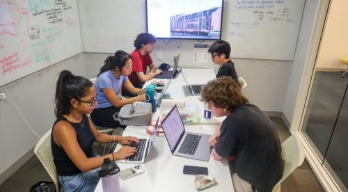 Students sit around a table, focusing intently on their laptops while working together