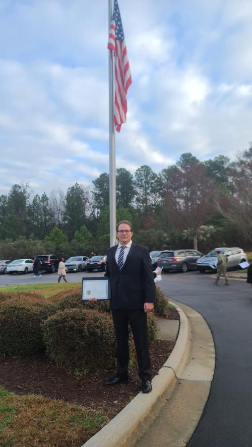 Christian standing in front of an American flag after becoming a United States citizen in December 2022.