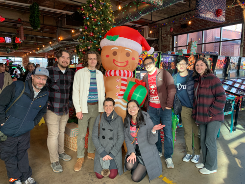 A group of Co-Lab employees pose together in front of an inflatable gingerbread man at the OIT End-of-Year celebration at Boxcar Bar and Arcade.